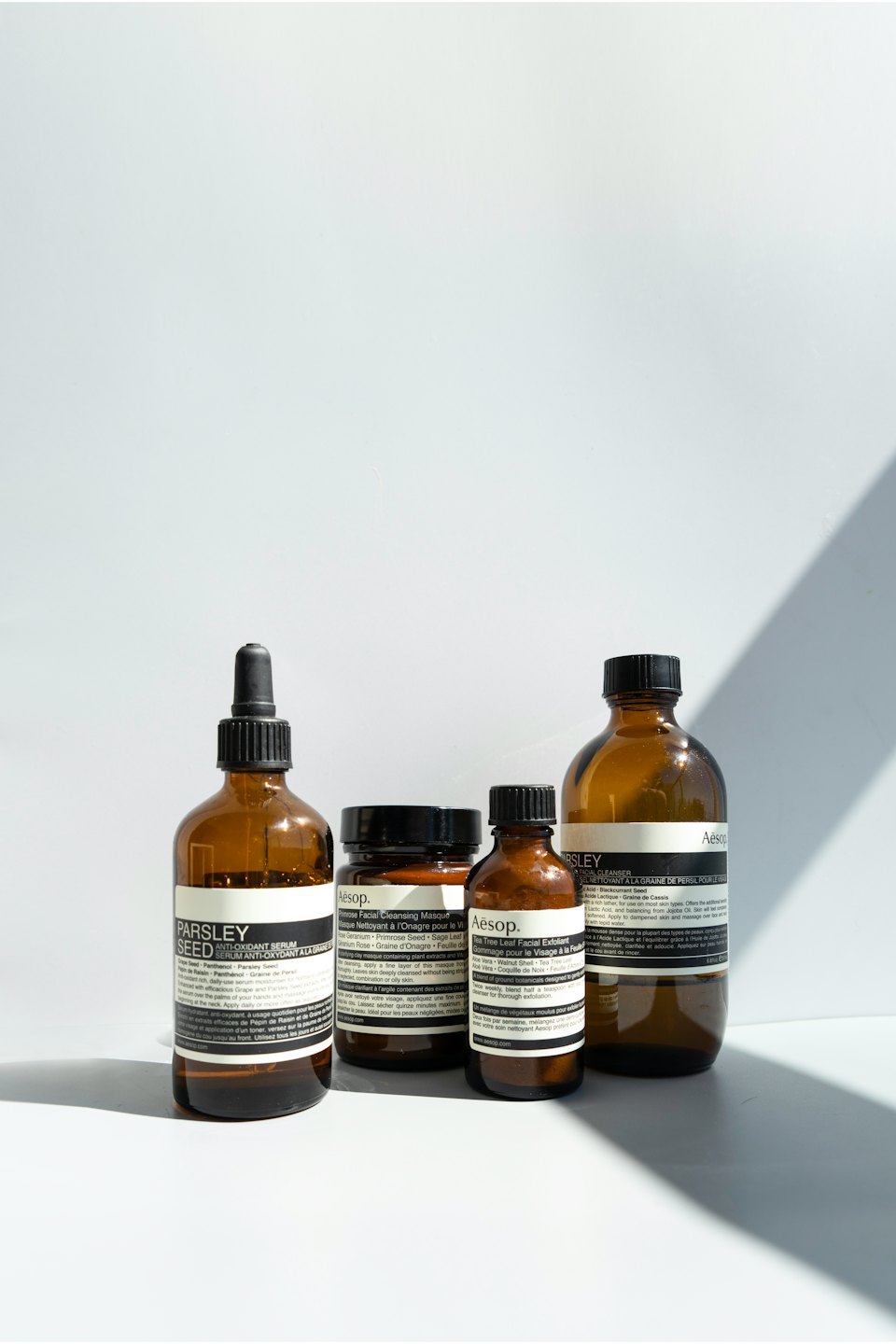 Four amber Aesop skincare bottles and jars on a white surface.